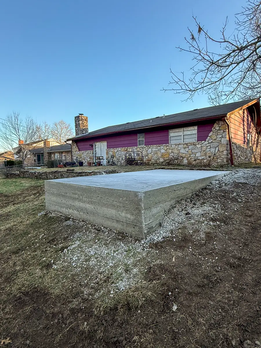 Raised concrete slab with formed edges beside a stone home