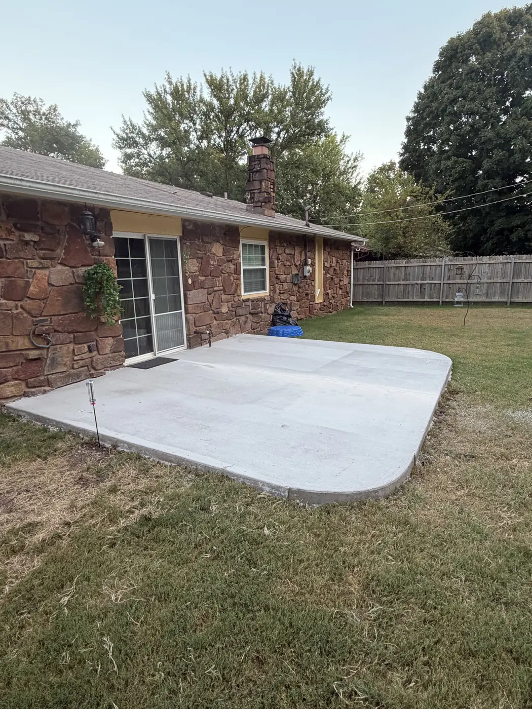 Finished concrete patio with rounded corners behind a stone home